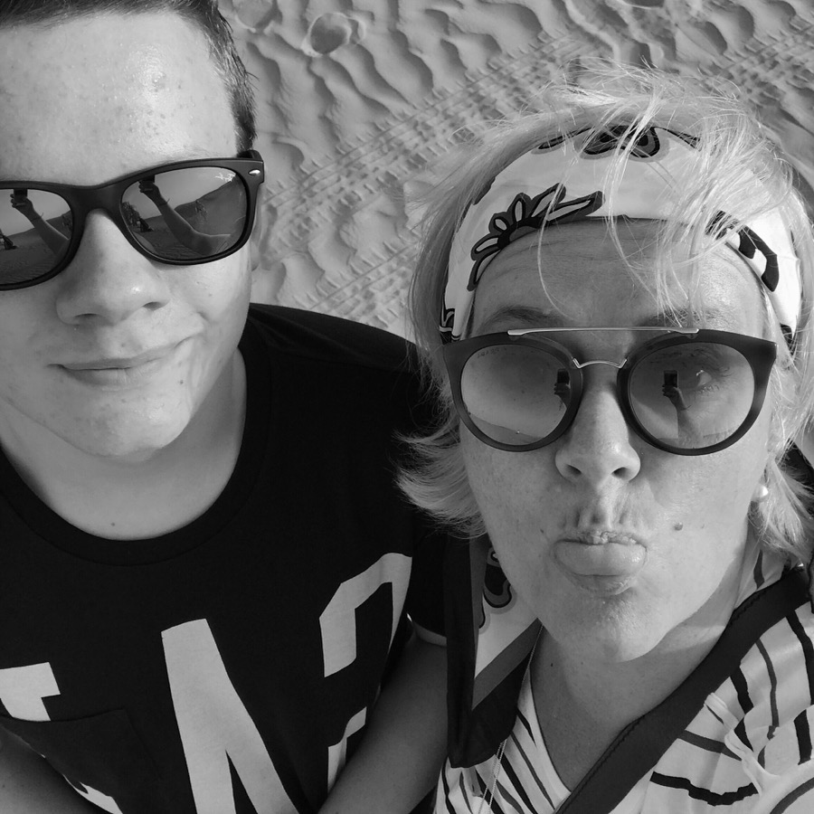 Schwarzweiß-Selfie von Andrea und ihrem Sohn am Strand, beide mit Sonnenbrille, dicht aneinander